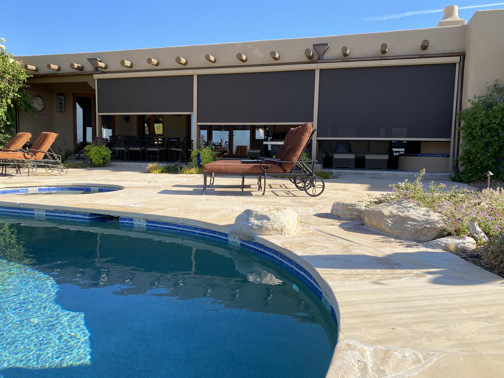 Charcoal exterior roller shades partially lowered over a poolside patio at a Southwestern-style home