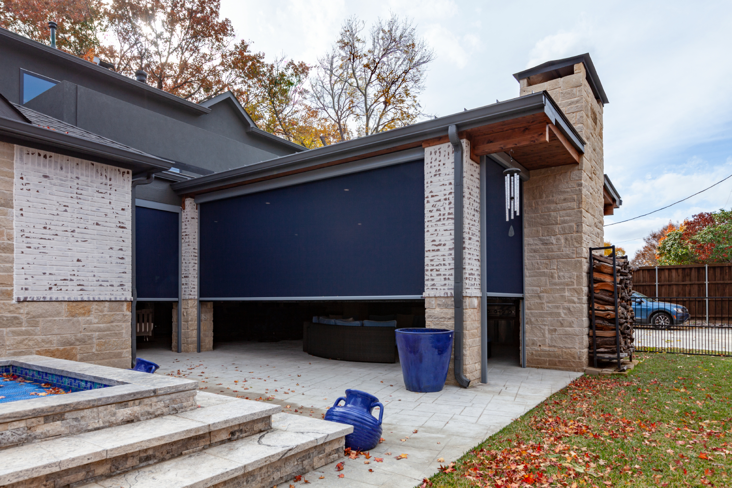 Navy motorized retractable shades partially lowered over a stone patio with a fireplace and pool beyond